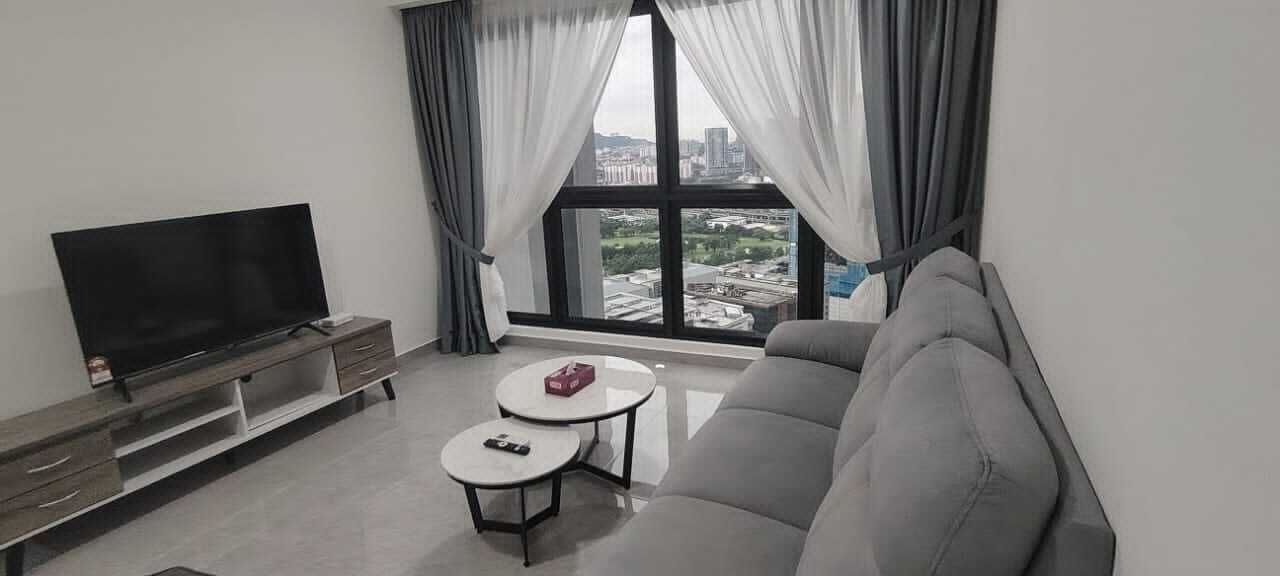 A modern living room with a flat-screen TV, a grey sofa, two small round tables, and a large window with curtains.