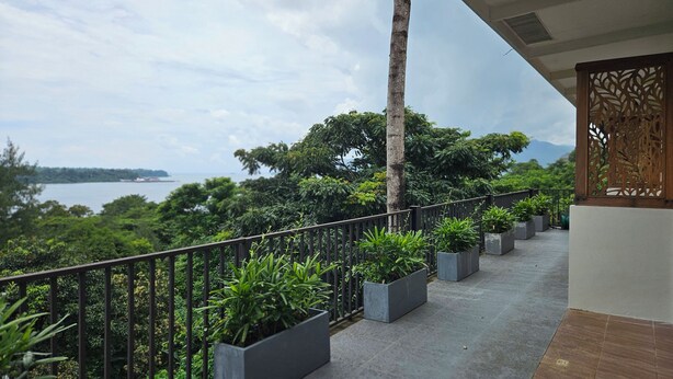 A balcony with a view of a body of water and greenery, a palm tree, and a decorative wooden panel. - Vine and Canopy (Morong)