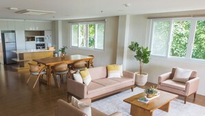 A spacious living area with a sofa, armchairs, a coffee table, and a dining table with chairs. There is a kitchen in the background with a refrigerator and microwave. - Vine and Canopy (Morong)