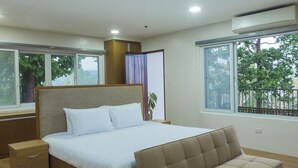 A modern bedroom with a bed, bedside tables, a sofa, and large windows offering a view of trees. - Vine and Canopy (Morong)