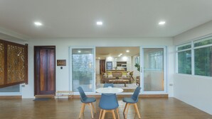 A spacious living area with a wooden floor, a round table with chairs, and a view into the kitchen through glass doors. - Vine and Canopy (Morong)