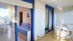 A modern room with a sofa, a dining table with chairs, and a large window with blinds. - Central Apartment With Terrace (San Michele al Tagliamento)