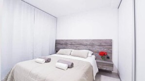Un dormitorio moderno con una cama, cabecera y una mesita con un florero.