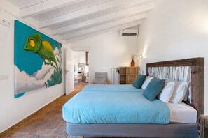 A bedroom with a bed, a large painting, and a wooden headboard. - Casa Papaya: Country House with Sea View, Wi-Fi, and Air Conditioning (Vila Nova de cacela)