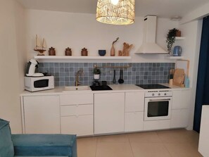 Una cocina compacta con armarios blancos, microondas, fregadero y horno. Hay elementos decorativos en los estantes sobre la encimera.