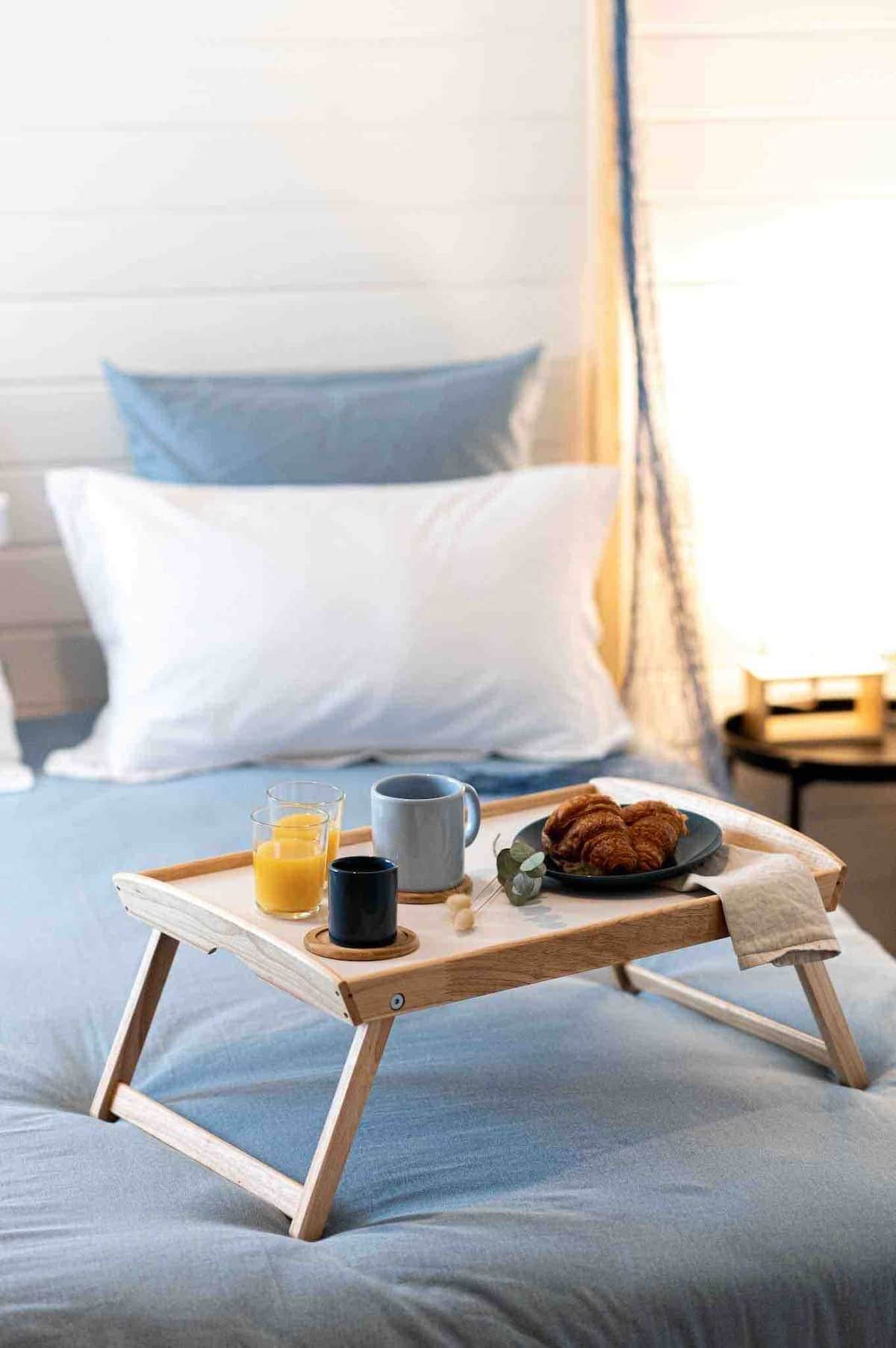 A bed with a wooden tray holding breakfast items, including croissants, a mug, and a glass of orange juice.