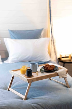 Ein Bett mit einem Holftablett, auf dem Frühstücksartikel wie Croissants, eine Tasse und ein Glas Orangensaft bereitstehen.