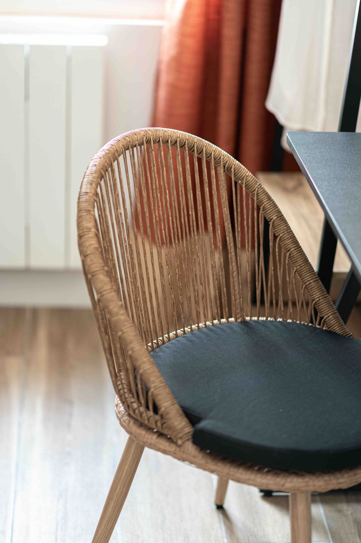 A wicker chair with a dark cushion, wooden legs, and a table beside it.