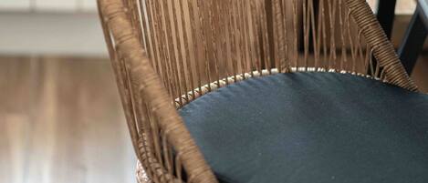 A wicker chair with a dark cushion, wooden legs, and a table beside it.