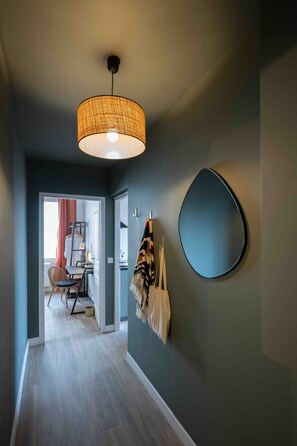 A hallway with a woven light fixture, a round mirror, and a coat rack with bags. - La Perle Verte - Large air-conditioned 2-bed flat, Agde centre (Agde)