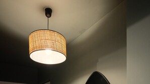Un couloir avec un luminaire tressé, un porte-manteau avec des sacs, et un miroir fixé au mur.