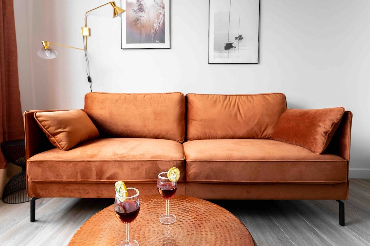 A modern living room with a brown leather sofa, two drinks on a round table, and artwork on the wall.