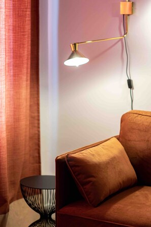 Ein Zimmer mit einem braunen Sofa, einem schwarzen runden Beistelltisch und einer modernen Stehlampe.
