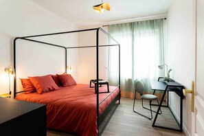 Un lit à baldaquin avec une couvre-lit rouge, un bureau avec une chaise et une lampe.