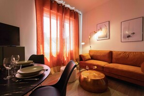 Un salon comprenant un canapé, une table à manger avec des chaises, un téléviseur et des œuvres d’art accrochées au mur.