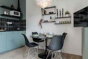 A modern kitchen with a dining area, featuring a round table, black chairs, and a hanging light fixture. - La Perle Verte - Large air-conditioned 2-bed flat, Agde centre (Agde)