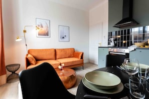 A modern living room with a sofa, a dining table set with plates and glasses, and a kitchen area with a stove and cabinets. - La Perle Verte - Large air-conditioned 2-bed flat, Agde centre (Agde)