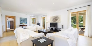 Een moderne woonkamer met witte meubels, een flatscreen televisie en kunstwerken aan de muren.
