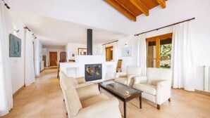 A spacious living room with a high ceiling, a fireplace, and a view of the outdoors. - Country House 'Son Aladern' with Mountain View, Wi-Fi and Air Conditioning (Illes Balears)