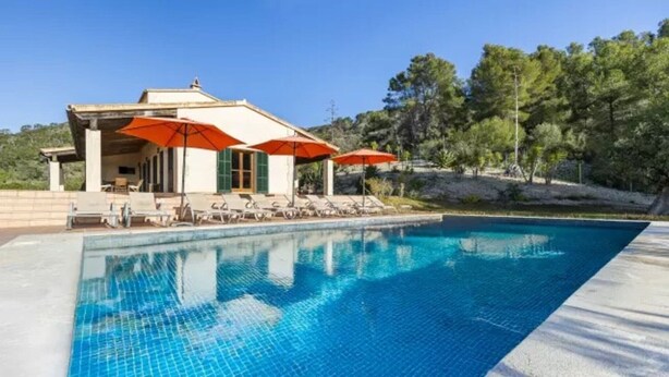 A swimming pool with lounge chairs and umbrellas, a building with a covered area, and trees in the background. - Country House 'Son Aladern' with Mountain View, Wi-Fi and Air Conditioning (Illes Balears)