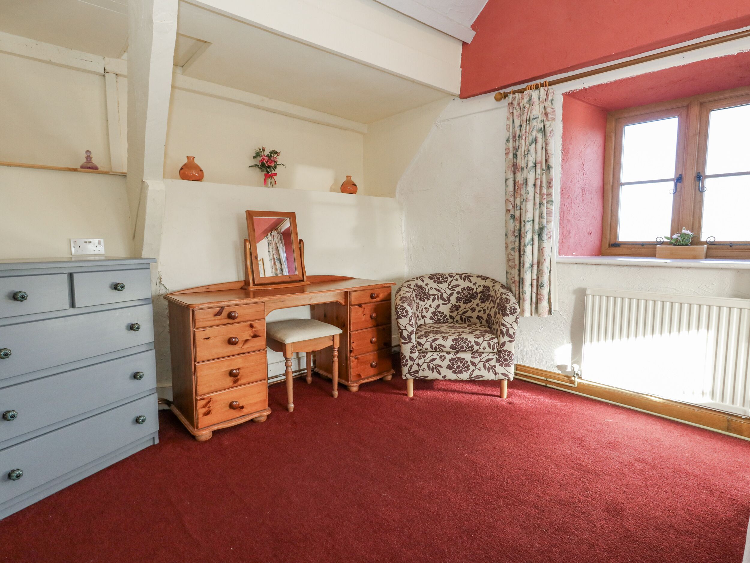 A room with a wooden desk, a chair, a dresser, a radiator, and a window with curtains.