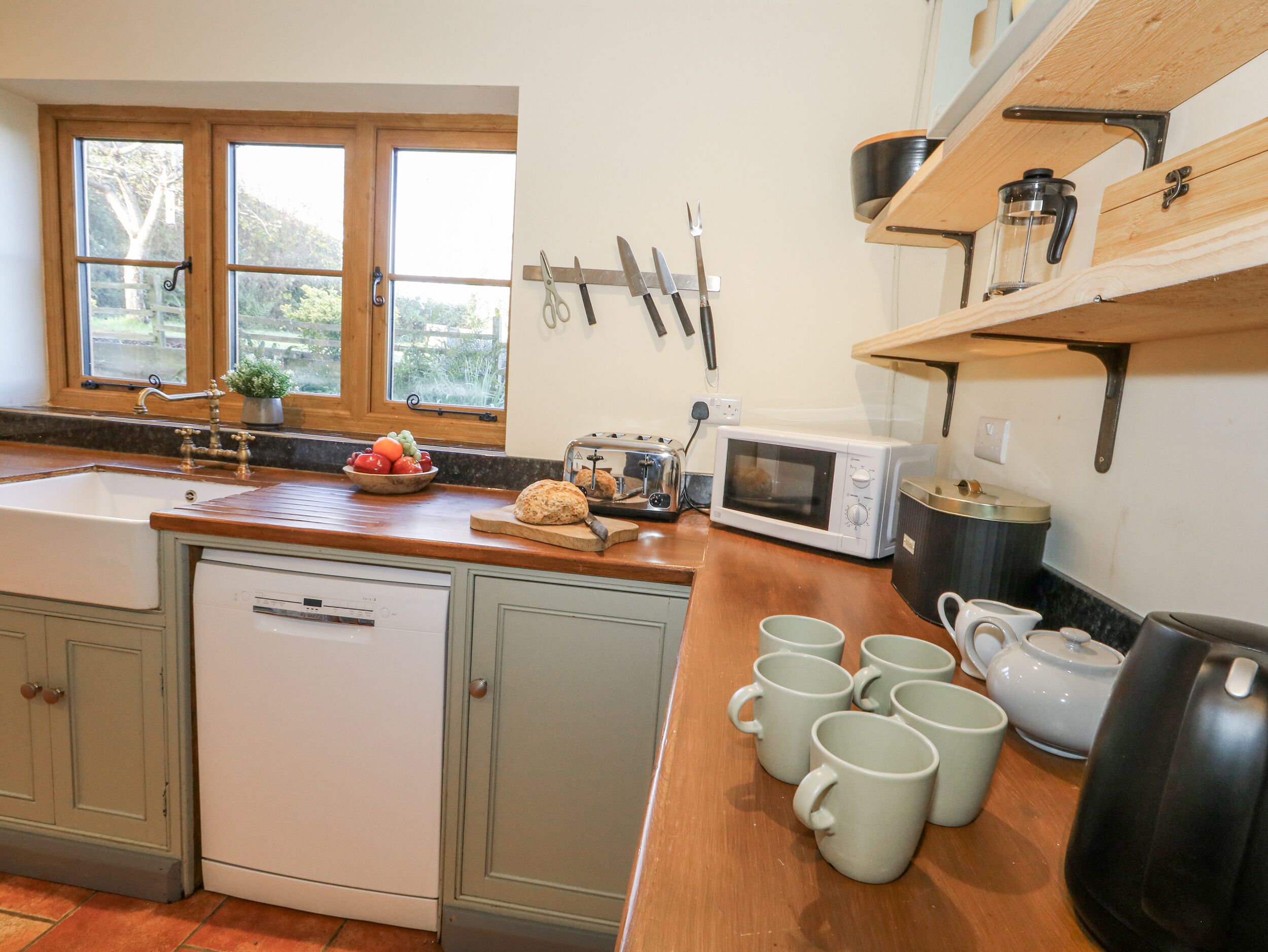 A kitchen with a wooden countertop, a sink, a microwave, and a toaster. There are several mugs and a teapot on the counter.