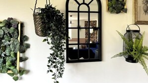 Un mur orné d’une fenêtre à cadre noir, de différentes plantes suspendues et d’un tableau encadré.