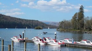 Un lac où plusieurs bateaux sont amarrés à un quai, entouré de collines et d’arbres.