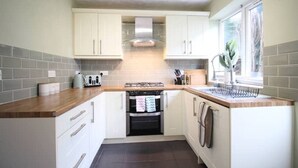Une cuisine compacte avec des meubles blancs, un four encastré, une cuisinière à gaz et une fenêtre qui laisse entrer la lumière naturelle.