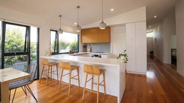 Una cocina moderna con una isla grande, taburetes de madera y lámparas colgantes.