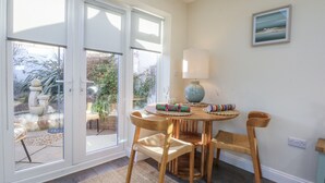 Un comedor con una mesa, sillas, una lámpara y vistas a un jardín exterior a través de puertas de vidrio.