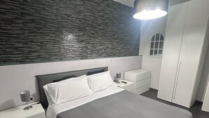 Une chambre à coucher moderne avec un grand lit, une table de chevet, une lampe, une armoire et une petite fenêtre.
