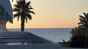 Un bâtiment moderne doté d’un balcon incurvé qui offre une vue sur une mer calme au coucher du soleil.