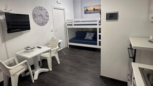 Une chambre avec un lit superposé, un bureau avec une chaise, une télévision et une horloge murale.
