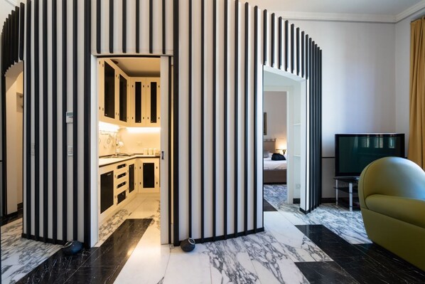Ett modernt hotellrum med ett litet kök, en tv och en sittgrupp.