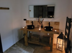 Ein Badezimmer mit zwei schwarzen Waschbecken, einem Spiegel darüber und einer kleinen, beleuchteten Kerze auf dem Waschtisch.