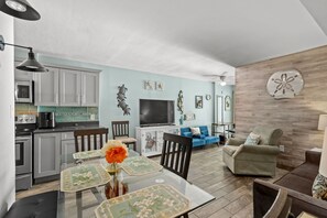 Una cocina moderna con armarios blancos, una mesa de comedor con individuales estampados y un sofá azul en la zona de estar.
