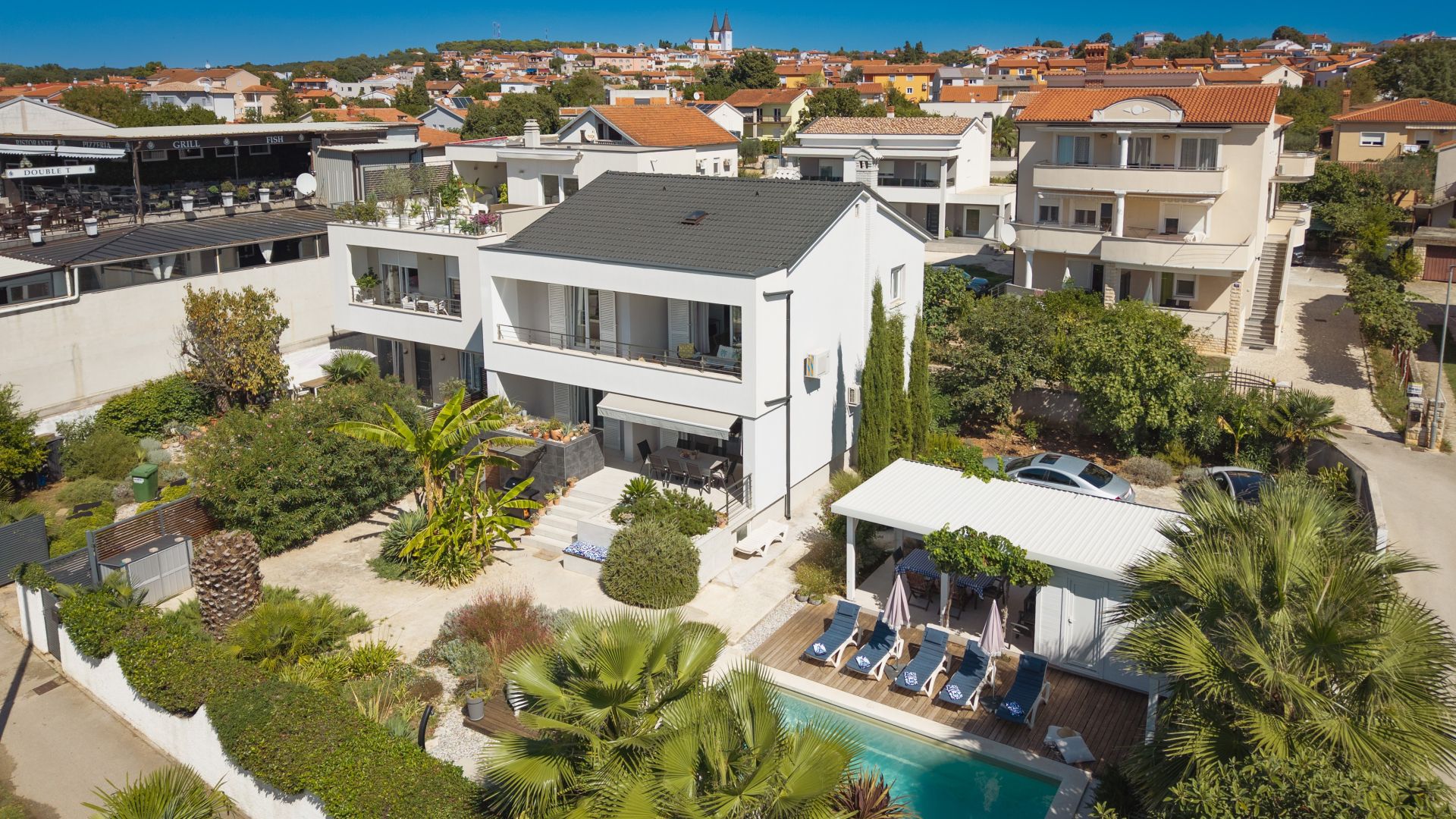 A modern two-story building with a rooftop terrace, a swimming pool, and a garden area.