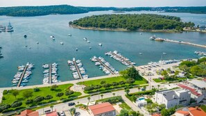 A marina with boats docked, a road leading to a building, and a green area with trees. - Villa La Vidas by Villas Guide (Medulin)