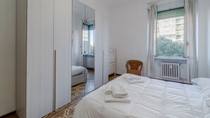 Een hotelkamer met een groot bed, een stoel, een kledingkast, een radiator en een raam met gordijnen.
