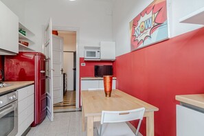 A compact kitchen with a red wall, white cabinets, a microwave, a refrigerator, and a dining table with a chair.