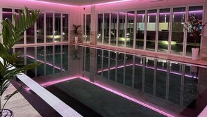 A modern indoor pool area with glass walls and pink ambient lighting. - Villas by Top Villas (Maminas)