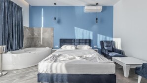 A modern bedroom with a large bed, a separate sitting area, a bathtub, and a flat-screen TV. - Villas by Top Villas (Maminas)