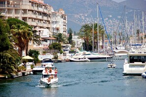 A marina with boats docked, a building with balconies, and palm trees. - 0130-MONTGRI House with private pool (Empuriabrava)