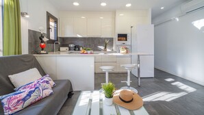 A modern kitchen with white cabinets, a dining area with a sofa and a table with a hat and plant. - 0130-MONTGRI House with private pool (Empuriabrava)