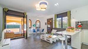 A modern kitchen with white cabinets, a dining area with blue chairs, and a seating area with a wicker sofa. - 0130-MONTGRI House with private pool (Empuriabrava)