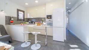 A modern kitchen with white cabinets, a built-in oven, and a refrigerator. There are two white bar stools and a small island with a sink. - 0130-MONTGRI House with private pool (Empuriabrava)