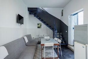 Ett kompakt bostadsutrymme med en soffa, ett matbord, stolar, en tv, en trappa och ett fönster.
