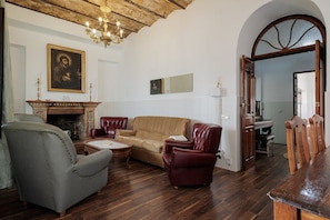 Uma sala de estar com lareira, sofás de couro, um candelabro e um espaço de jantar com móveis de madeira.