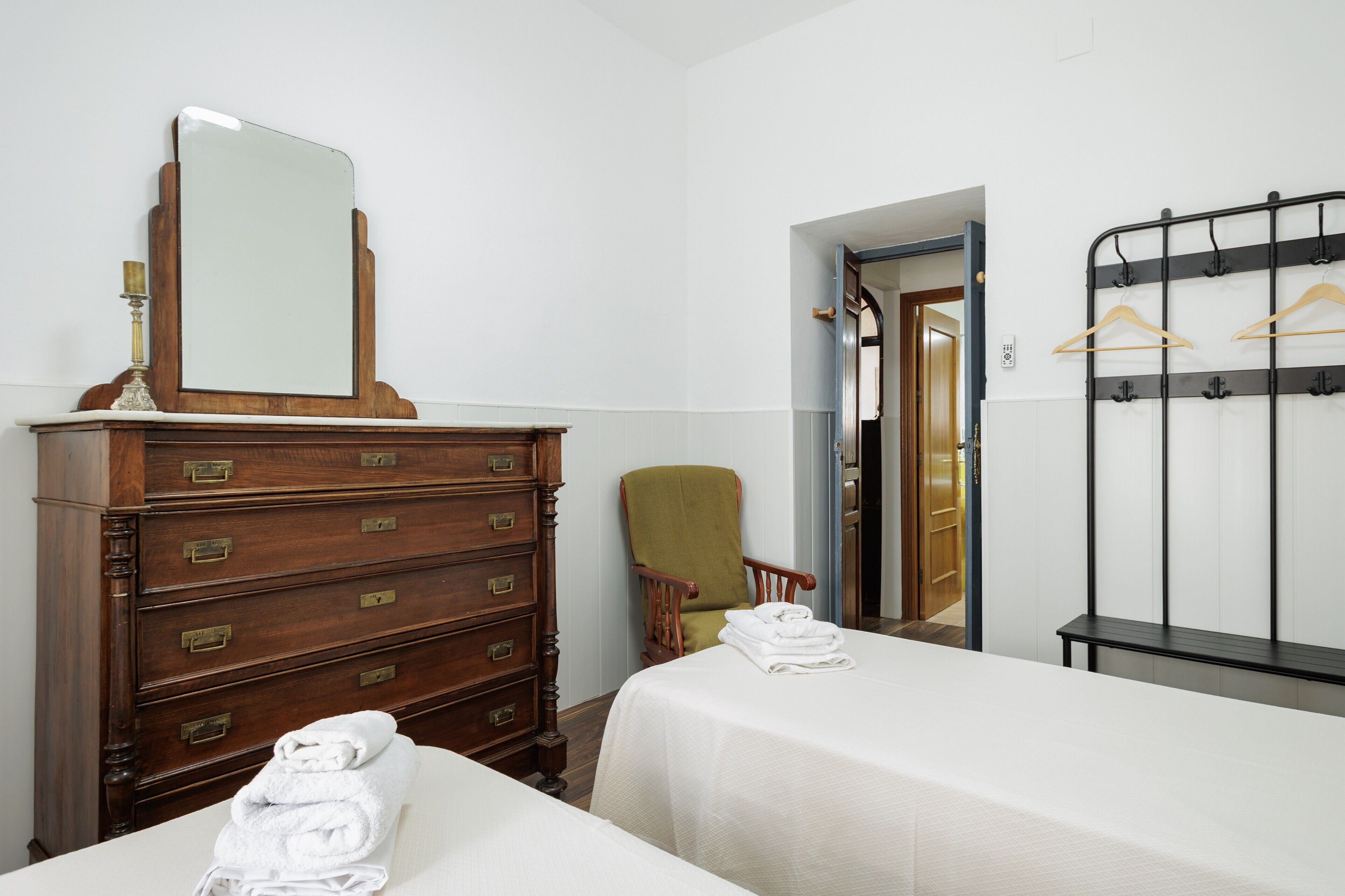 Een hotelkamer met twee bedden, een houten dressoir met lades, een stoel, een spiegel en een kapstok.